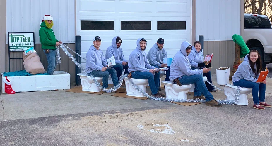The Top Tier crew in a chaotic Christmas skit: toys on the floor, someone asleep on the couch, an elf costume.