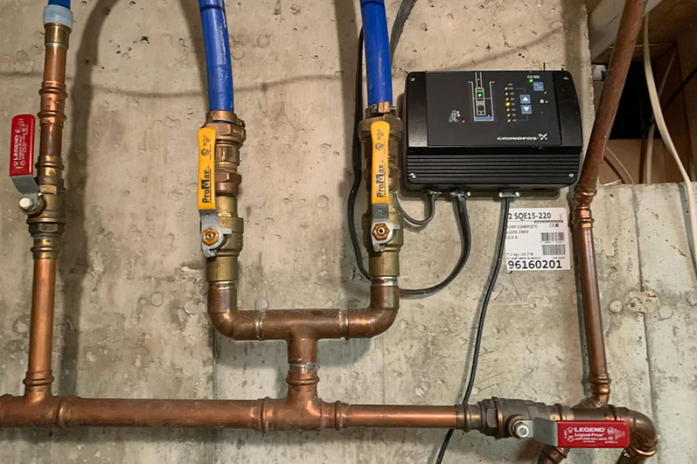Copper and blue PEX pipe, shutoff valves and a pump control mounted on a concrete wall.